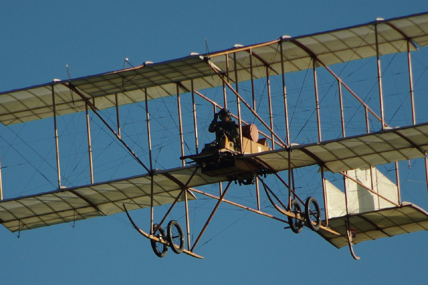 Sur fond de ciel bleu vole la réplique d’un avion biplan Bristol Boxkite de 1909, avec ses deux ailes portantes superposées, sa structure en bois et sa voilure de toile fixée par de nombreux haubans.